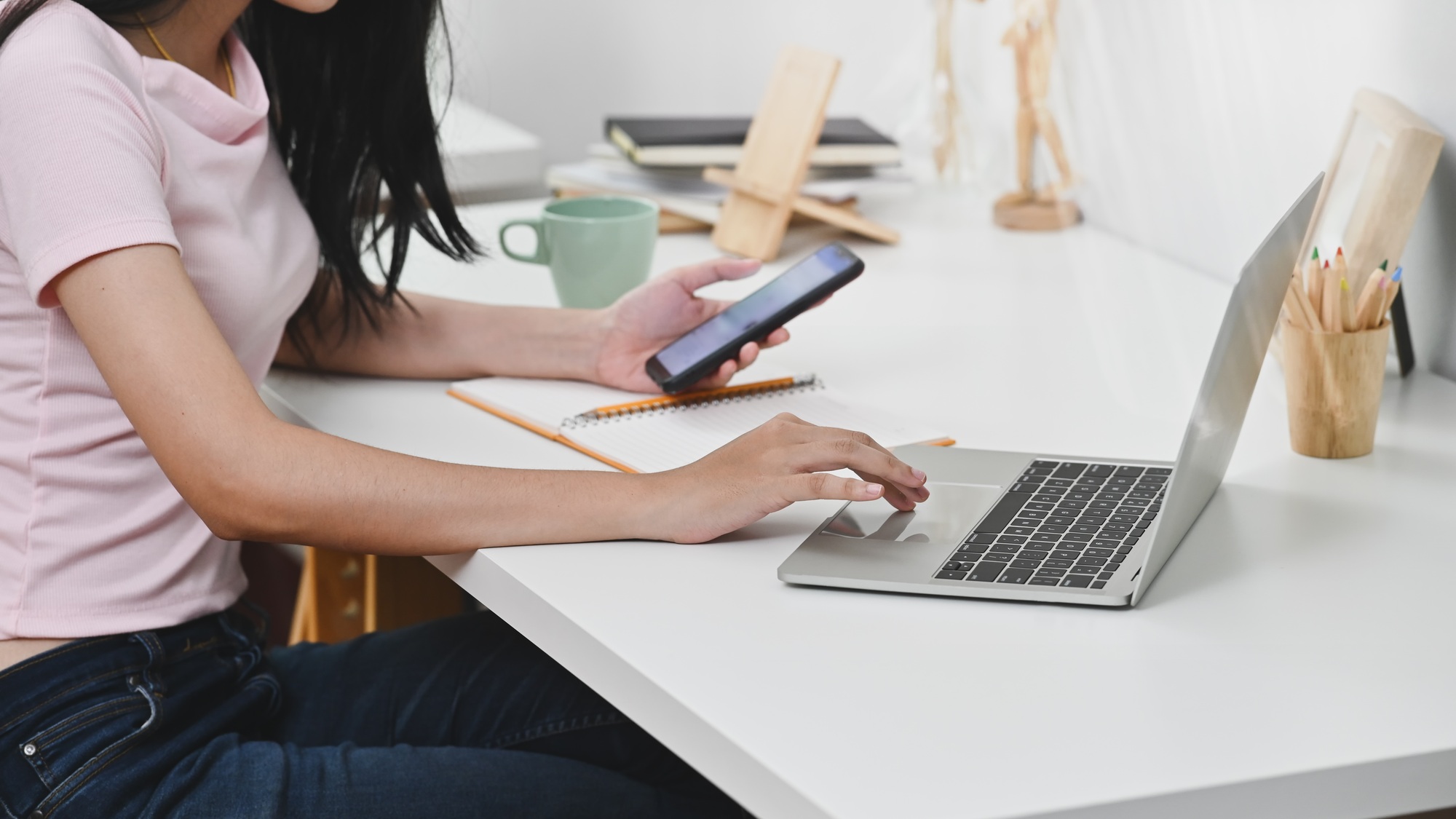 Cropped shot young woman using laptop and smartphone on workplace.